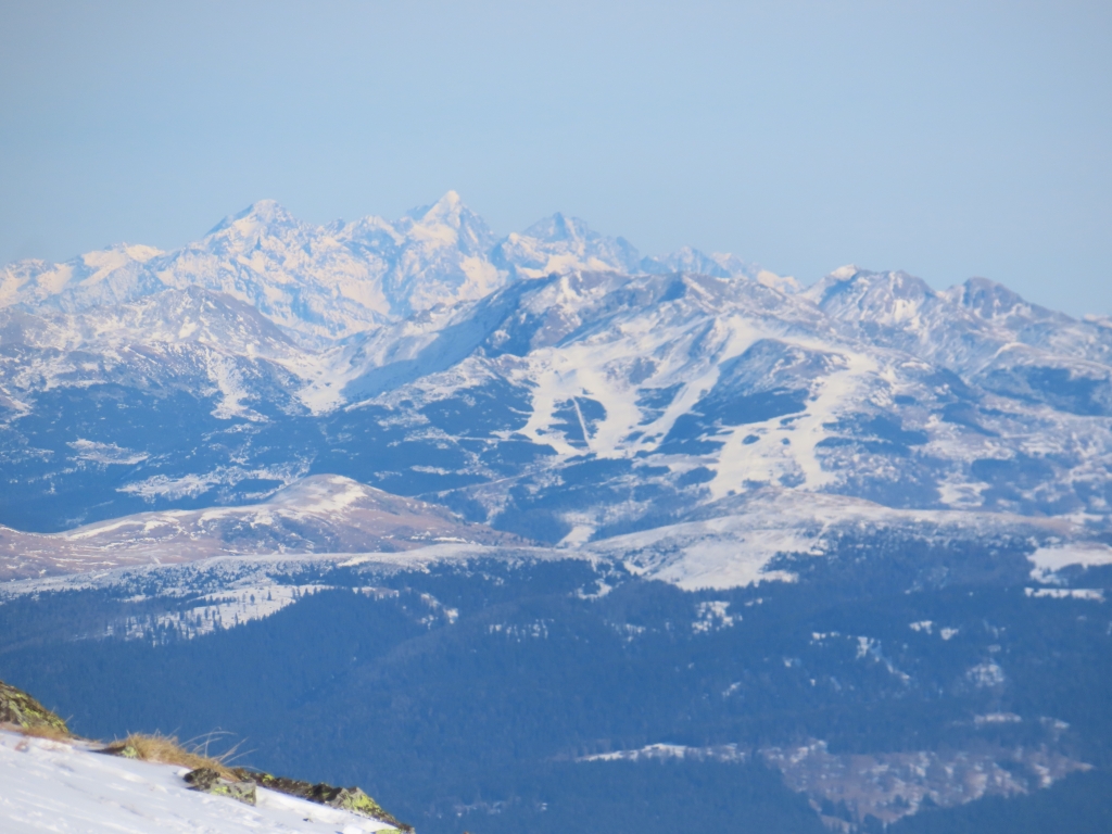 Zoom auf das Skigebiet Reinswald. Dahinter in großer Entfernung die Gipfel der Rieserfernergruppe.