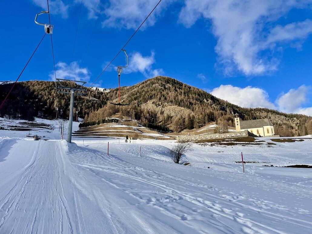 Das Trasse, rechts die Kirche San Peter mit Friedhof. Die Schlittelpiste ist hier gleich direkt daneben zu erkennen.