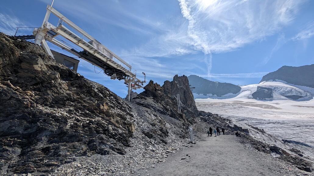 Ein "in der Luft schwebender" Schlepplift nach Gletscher Schwund. Wenn ich das richtig sehe wird der Gletscher Lift aber trotzdem von hier angetrieben, und das erste kurze Seil treibt die Umlenkscheibe weiter oben an, die wiederum den eigentlichen Gletscher Schlepplift antreibt.