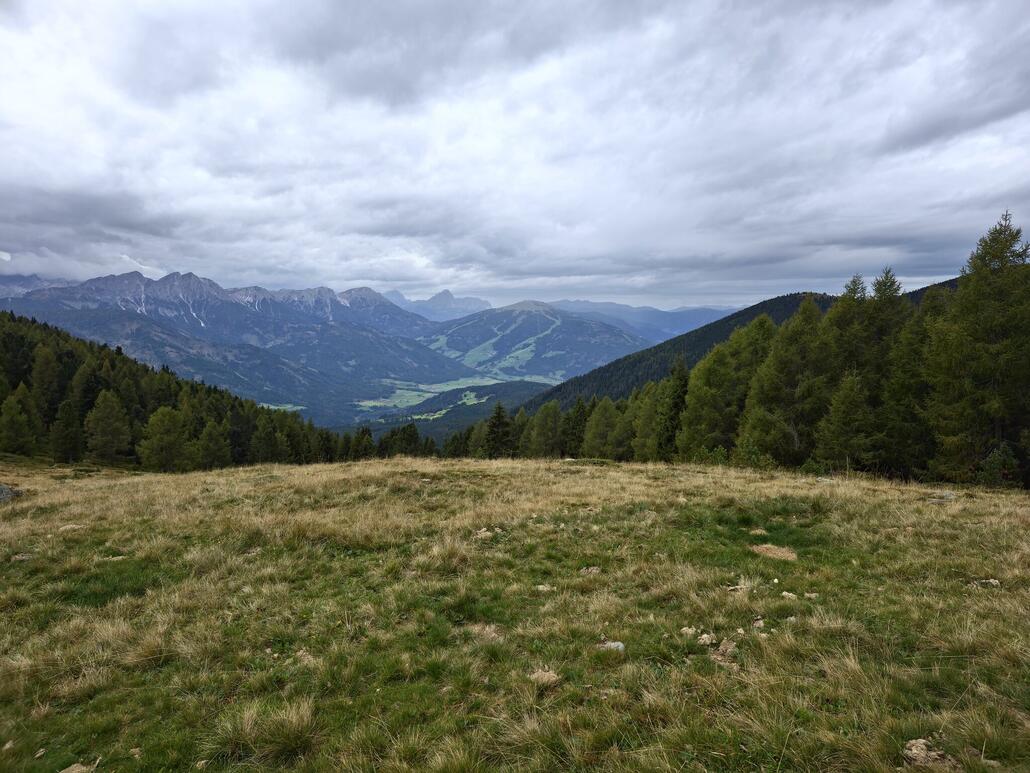 Angelangt bei der aussichtsreichen Sitzbank. Blick nach Olang mit Kronplatz sowie den ersten Bergen der Dolomiten. Mittlerweile ist eine dunkle Bewölkung aufgezogen.